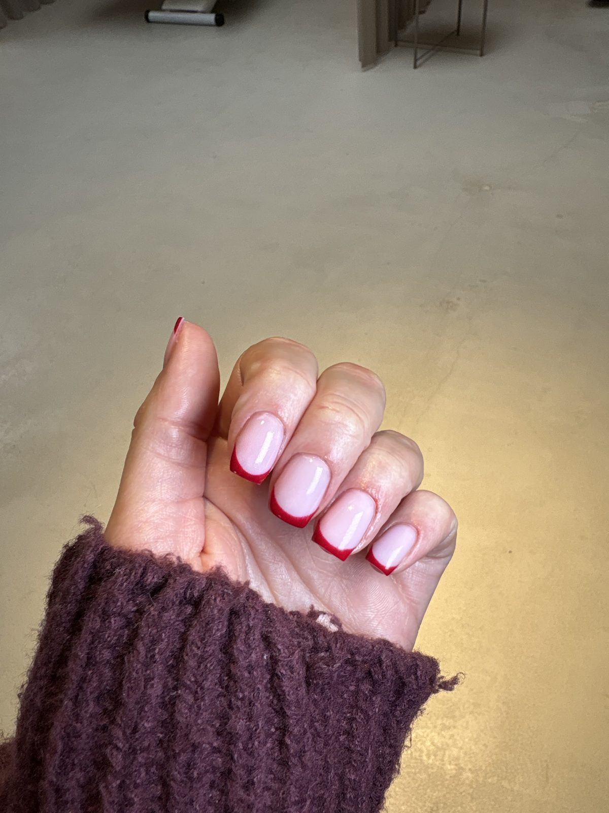 Rode French op korte nagels, de hand in een bordeauxrode trui